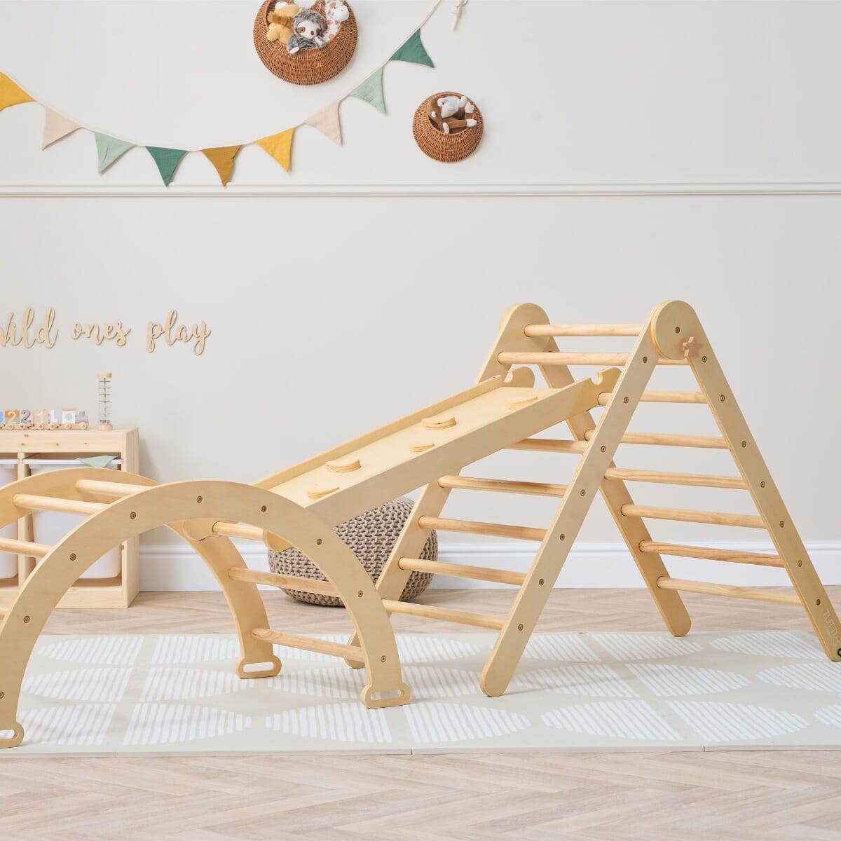 Scala Montessori Pikler Climbing Frame in natural wood shown in a playful nursery setup with soft furnishings and open-ended accessories