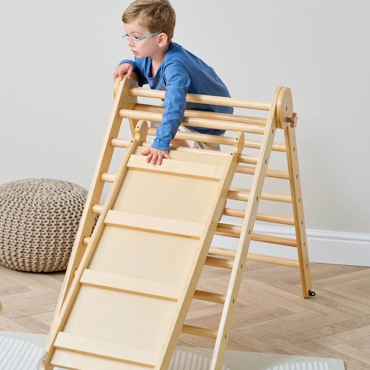 Child scaling the Scala Montessori Pikler climbing frame with slide in natural finish, supporting active play and independent climbing skills