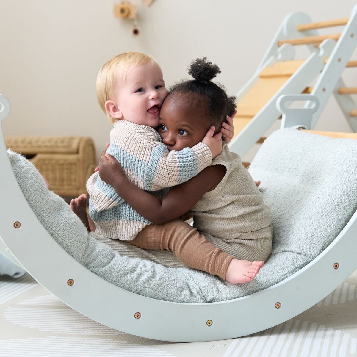 Toddlers on the Scala Pikler rocking frame with boucle sea mist cushion, capturing warmth, closeness, and shared joy in play