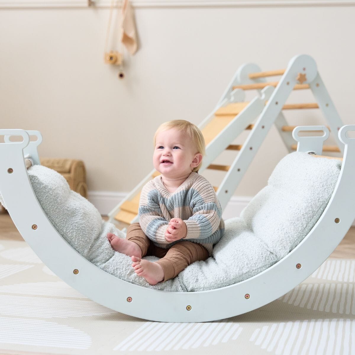 Toddler sitting on the Scala Pikler rocking frame with boucle sea mist cushion, styled in a calm nursery