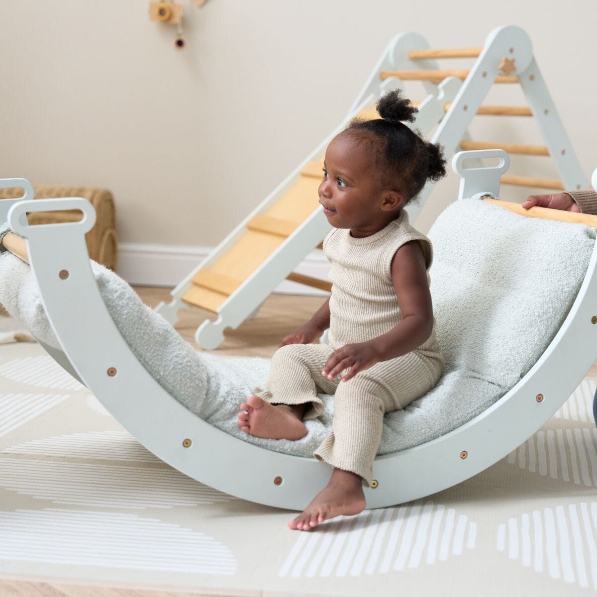 Toddler seated on the Scala Pikler rocking frame with boucle sea mist cushion, enjoying the soft support and gentle rocking motion