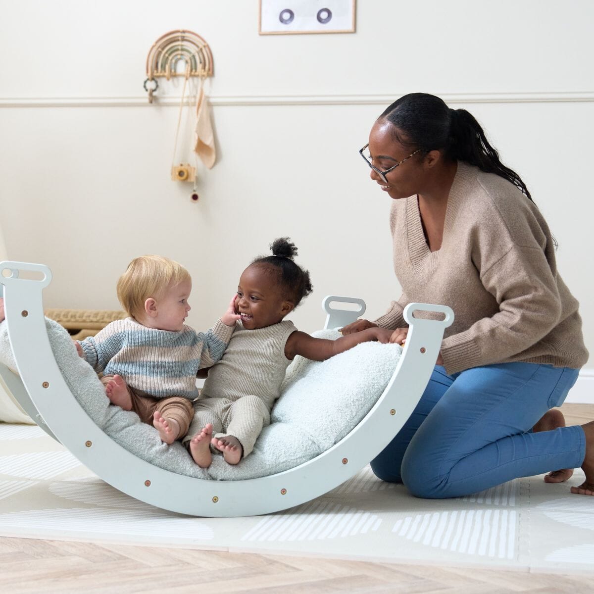Adult and two toddlers interacting on the Scala Pikler rocking frame with boucle sea mist cushion, supporting connection and co-play