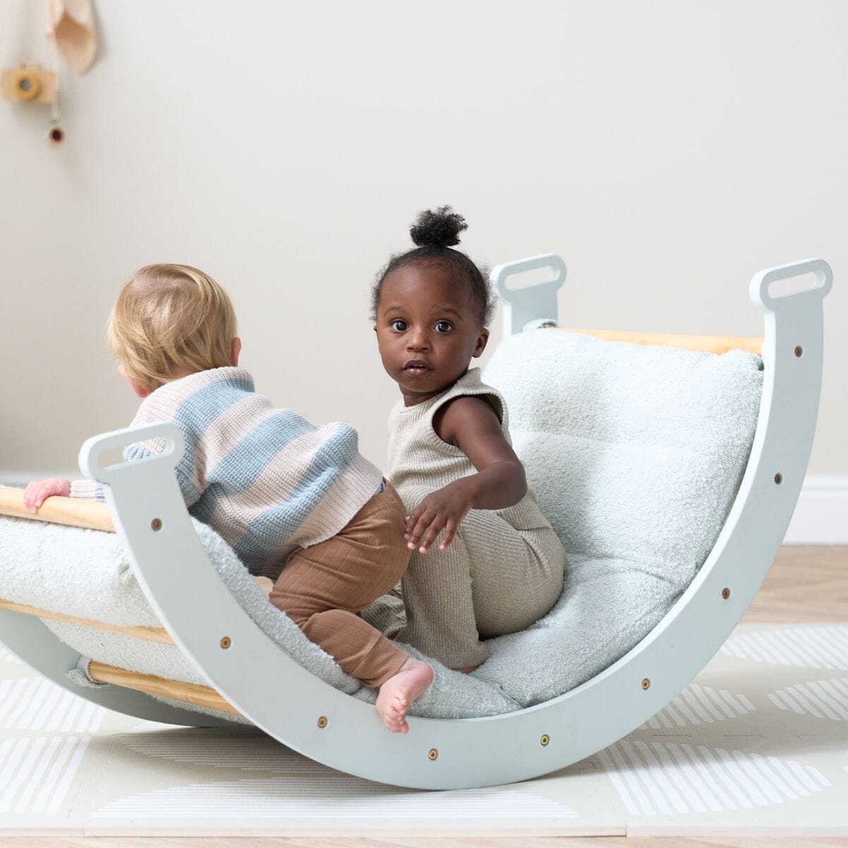 Two toddlers playing on the Scala Pikler rocking frame with boucle sea mist cushion, highlighting balance, social play, and movement.