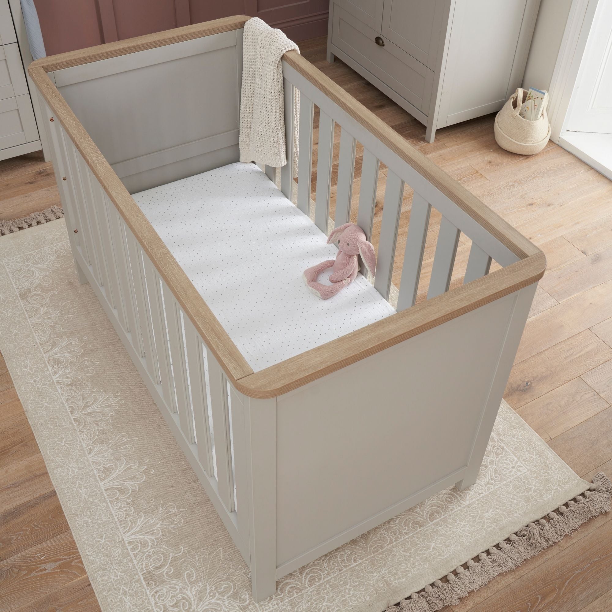 verona cot bed in dove grey and oak - aerial view showcasing the cot bed’s clean lines, soft rounded edges and oak top rails in a styled nursery setting
