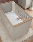 verona cot bed in dove grey and oak - aerial view showcasing the cot bed’s clean lines, soft rounded edges and oak top rails in a styled nursery setting
