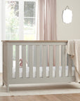 Verona cot bed in dove grey and oak placed in a bright nursery room, designed to convert into toddler and sofa modes for extended use.