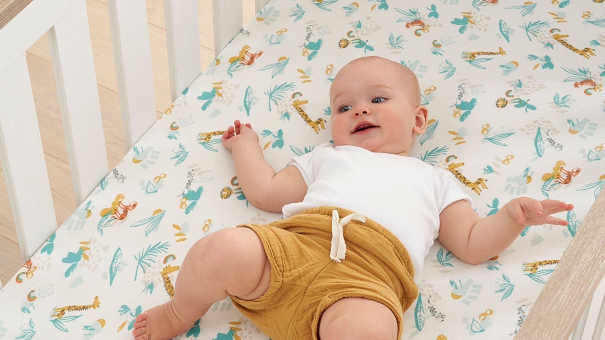 Baby giggling in their cot bed, with minimal baby bedding following safe sleep advice.