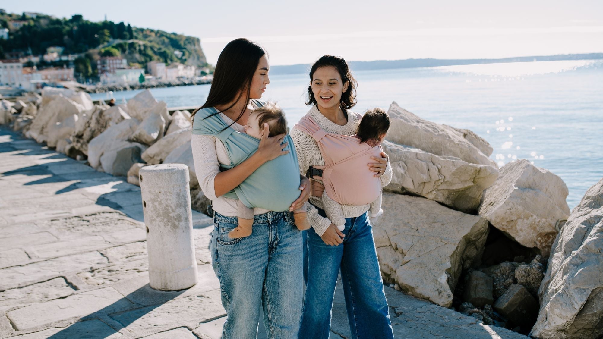 Two mums walking down the beachside, carrying their babies in their Boba Bliss baby carriers.