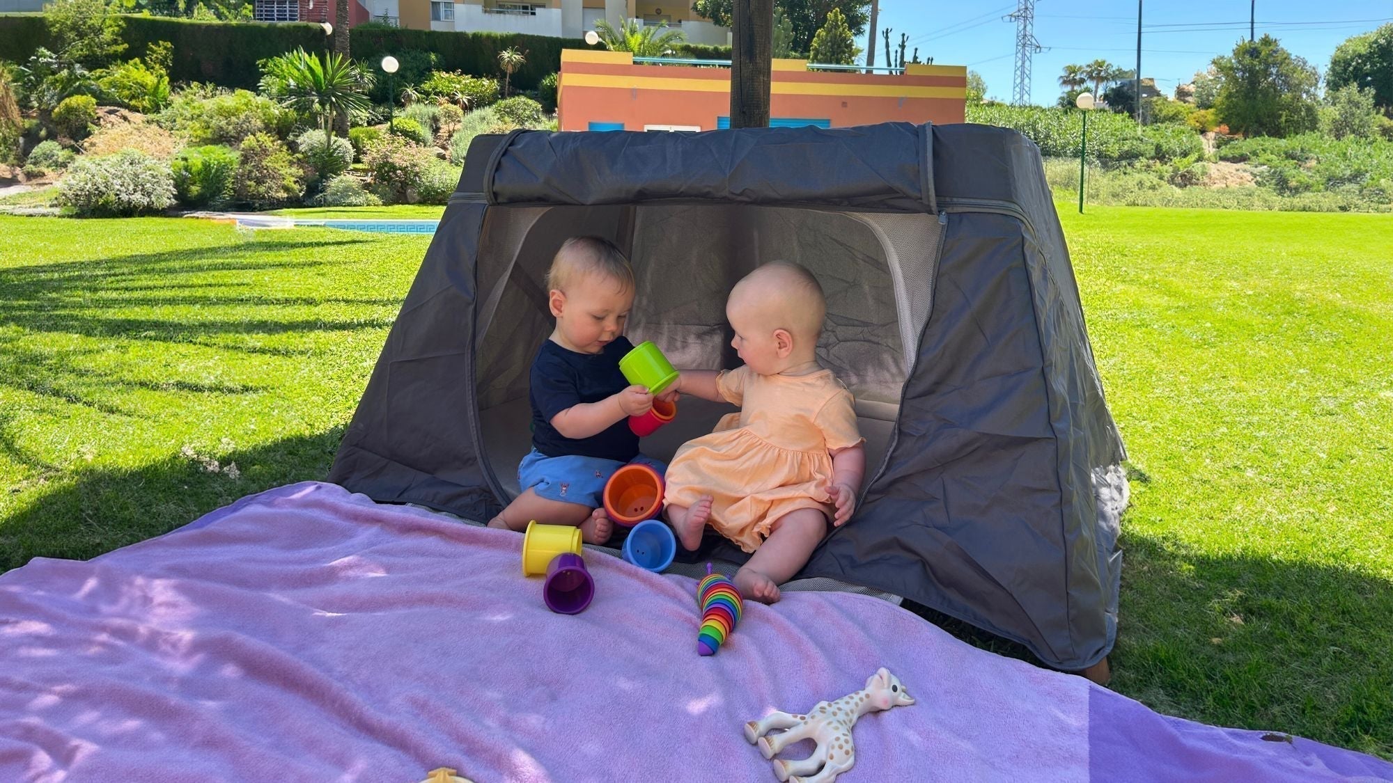 Babies playing in their CoZee Go travel cot and playpen, outside in the sun in a resort in Spain. The shade cover keeping them protected from the sun.
