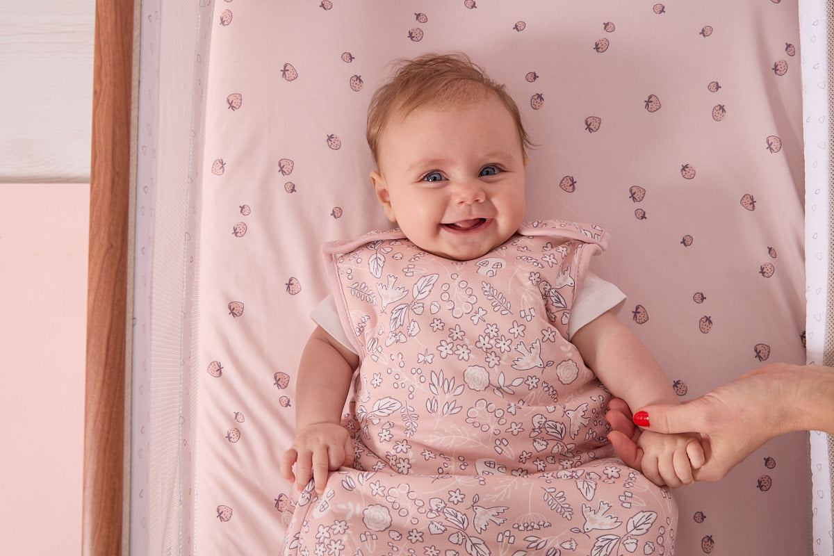 parent holding babies hand as they lie in a bedside crib on the tiny tails bedside crib fitted sheets