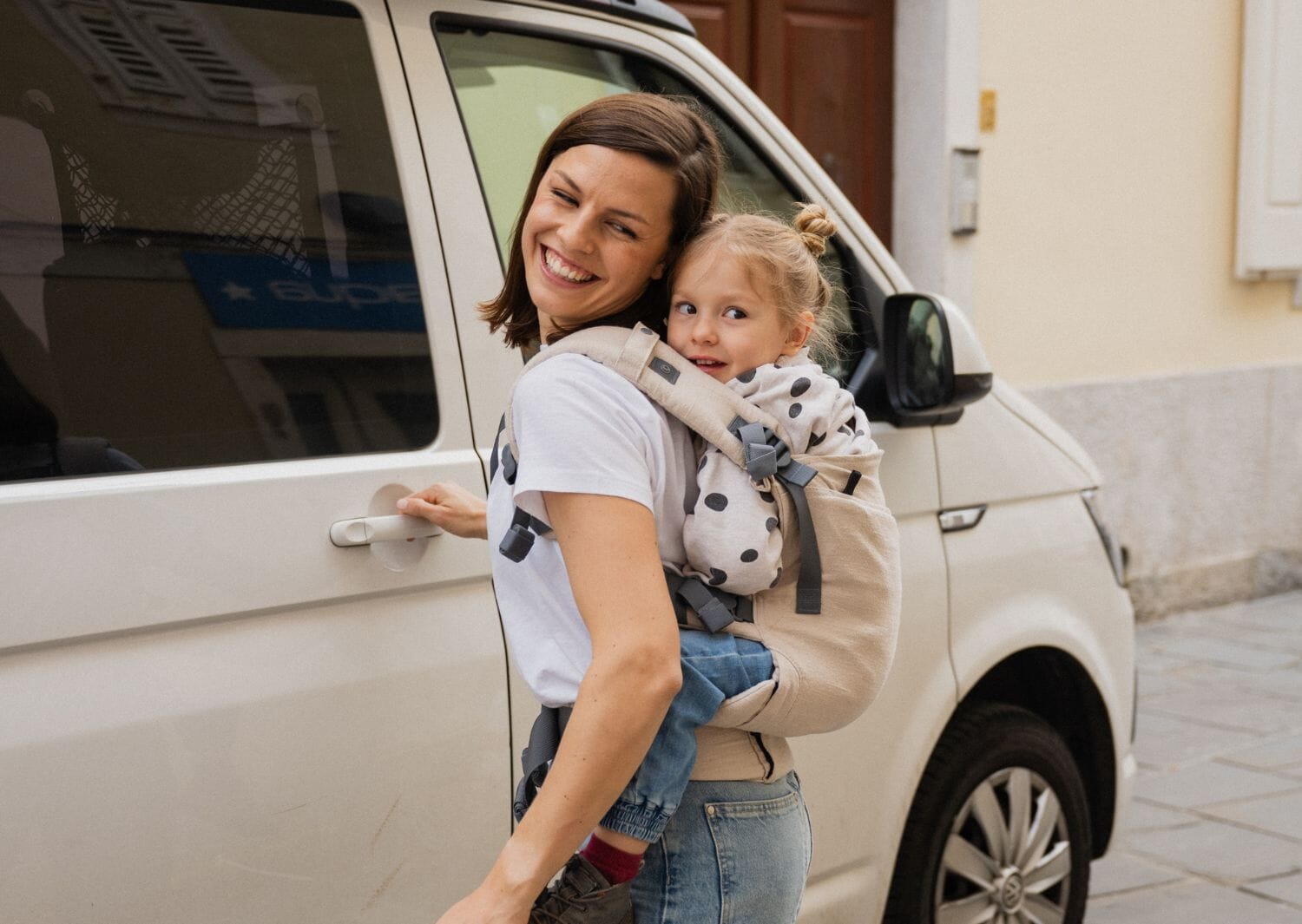 mum and daughter smiling in a boba x baby carrier next to a white van