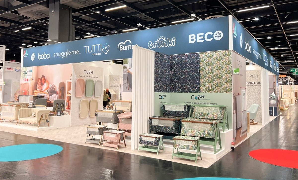 Tutti Bambini stand at Kind + Jugend 2024 featuring CoZee bedside cribs, Cushi changing mats, and vibrant limited-edition fabric designs.