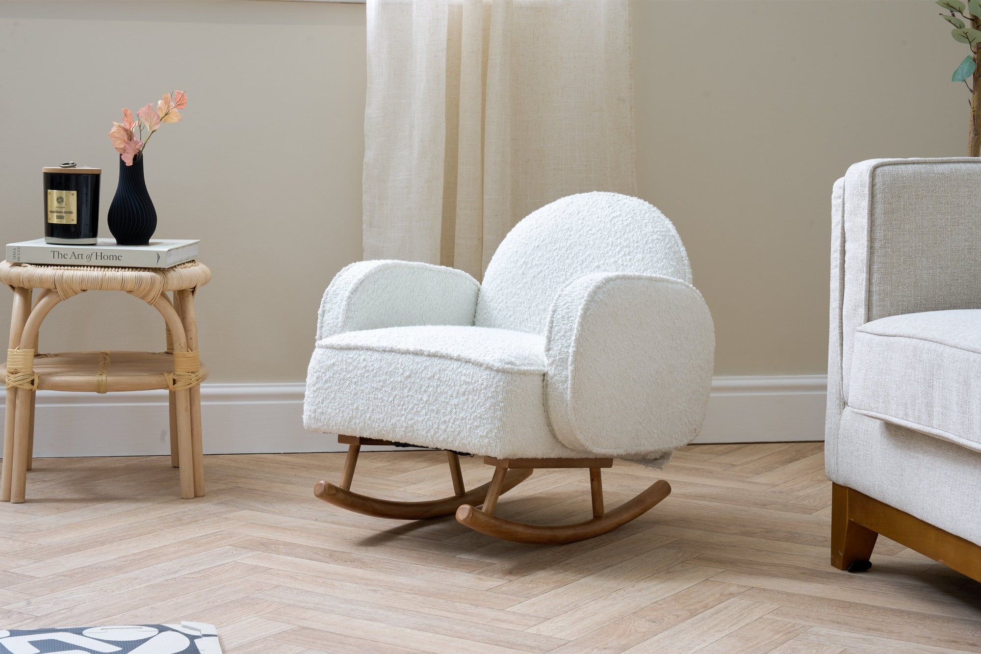 Lifestyle view of the boucle fresh cream Micah Mini Me Rocking Chair with smooth wooden rocking base, styled beside a rattan side table