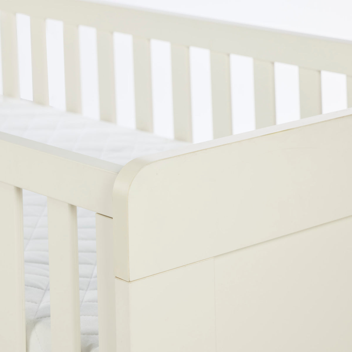 A close up corner view of the Alba cot bed in cashmere in a white background.