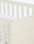 A close up corner view of the Alba cot bed in cashmere in a white background.