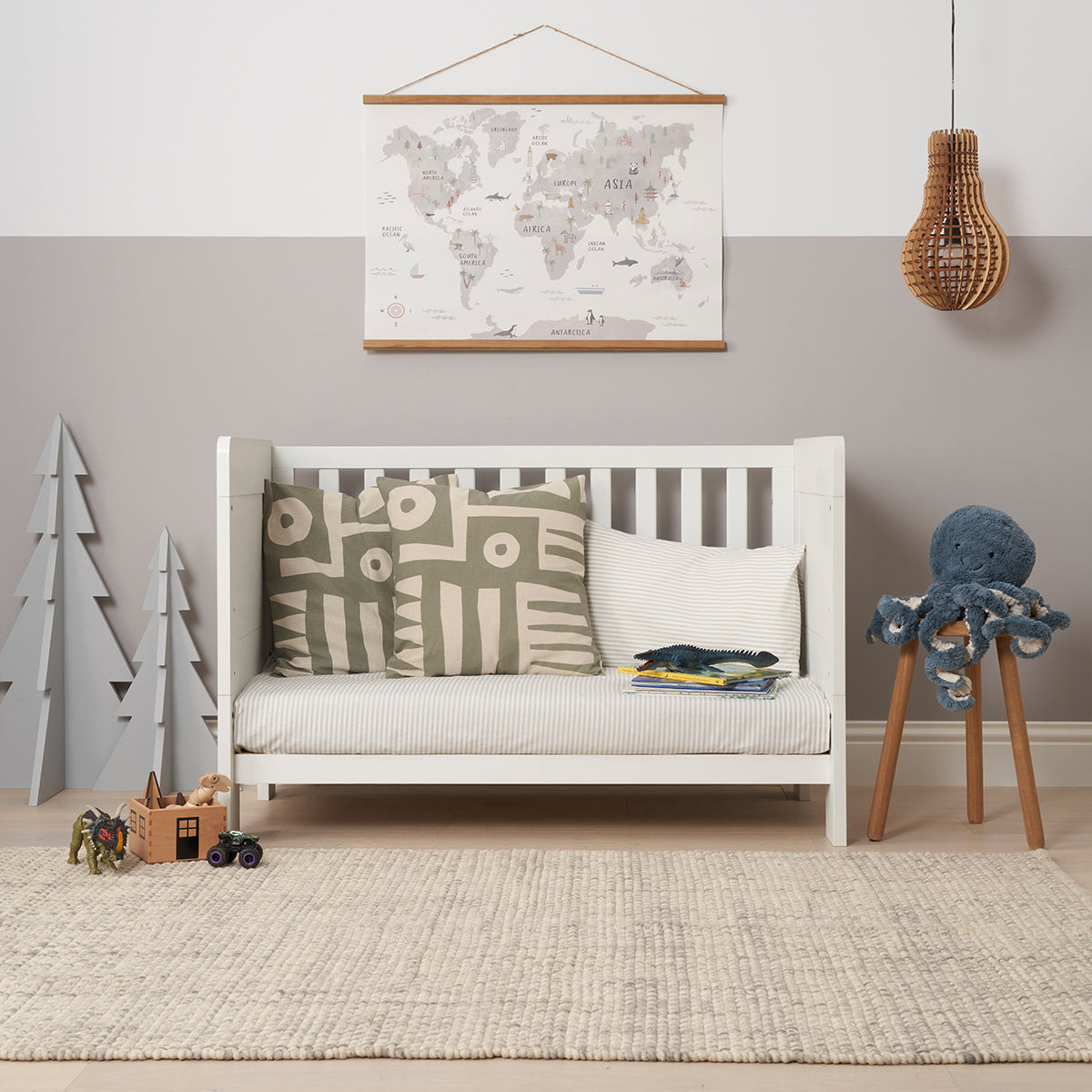 Alba Mini Cot bed in sofa mode with patterned cushion in a room with toys and a world map on the wall.