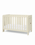 A side view of the Alba mini cot bed in cashmere with a mattress on a white background.