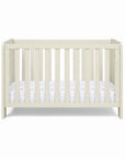 The Alba mini cot bed in cashmere with a mattress on a white background.