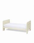 An angle view of the Alba mini cot bed in cashmere converted into a toddler's bed with a mattress on a white background.