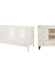 A white convertible cot bed and matching three-drawer changing table with open shelves, shown on a plain white background.