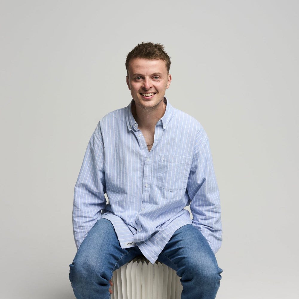 Alex Hobern sitting on a white cylindrical object against a plain background