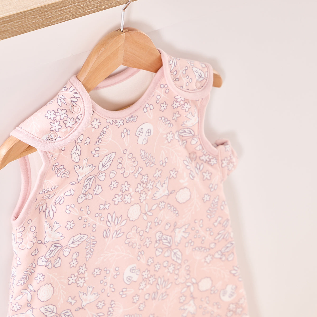 Close-up of Tiny Tails sleep bag on hanger, showing delicate woodland print and popper detail on soft pink breathable fabric