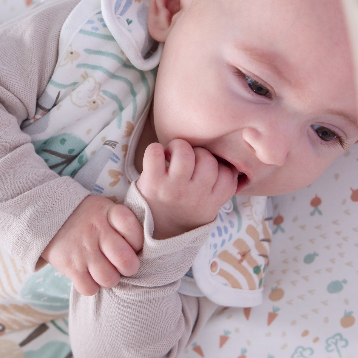 Baby lying on Good Life sleep bag with soft countryside print, exploring the gentle textures in a calm and cosy moment