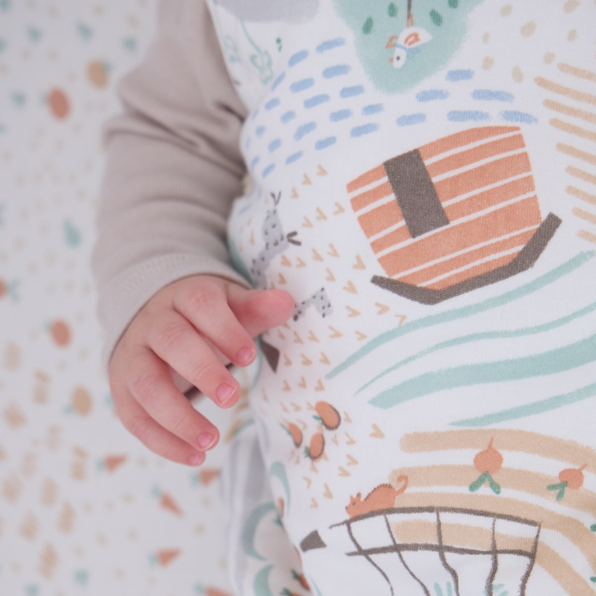Close-up of baby’s hand resting on the Good Life sleep bag, highlighting the soft fabric and playful farmyard pattern details