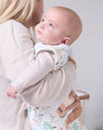 Mother holding baby dressed in the Good Life baby sleep bag, showing snug fit and soft pastel countryside pattern