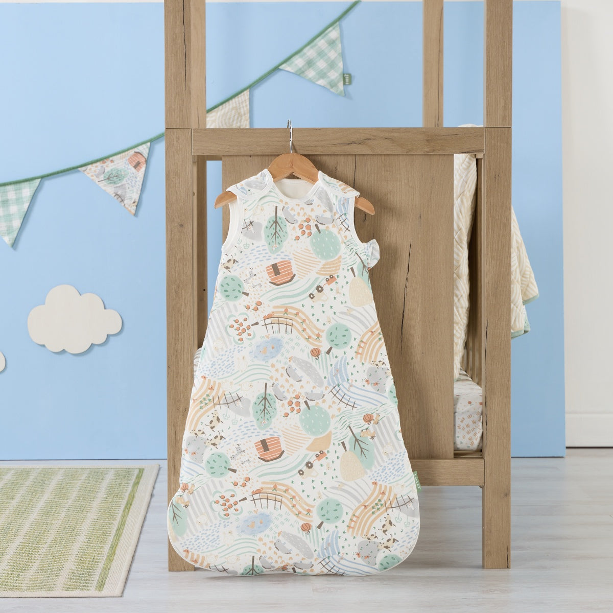 Good Life baby sleep bag hanging in a light nursery with blue wall and bunting, featuring calming farmyard print