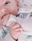 Close-up of baby wearing the Good Life sleep bag, gently chewing sleeve while lying on matching countryside themed sheet
