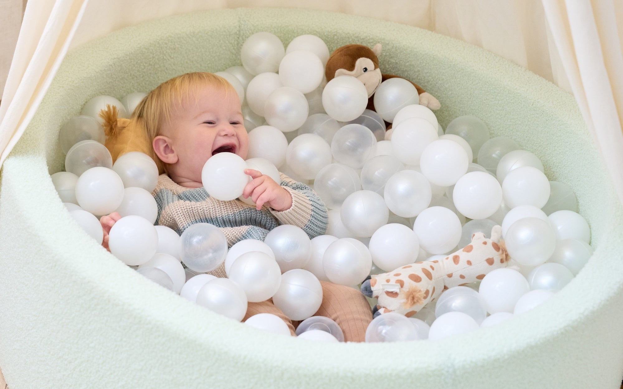 Smiling baby playing in a mint green ball pit filled with white and clear balls