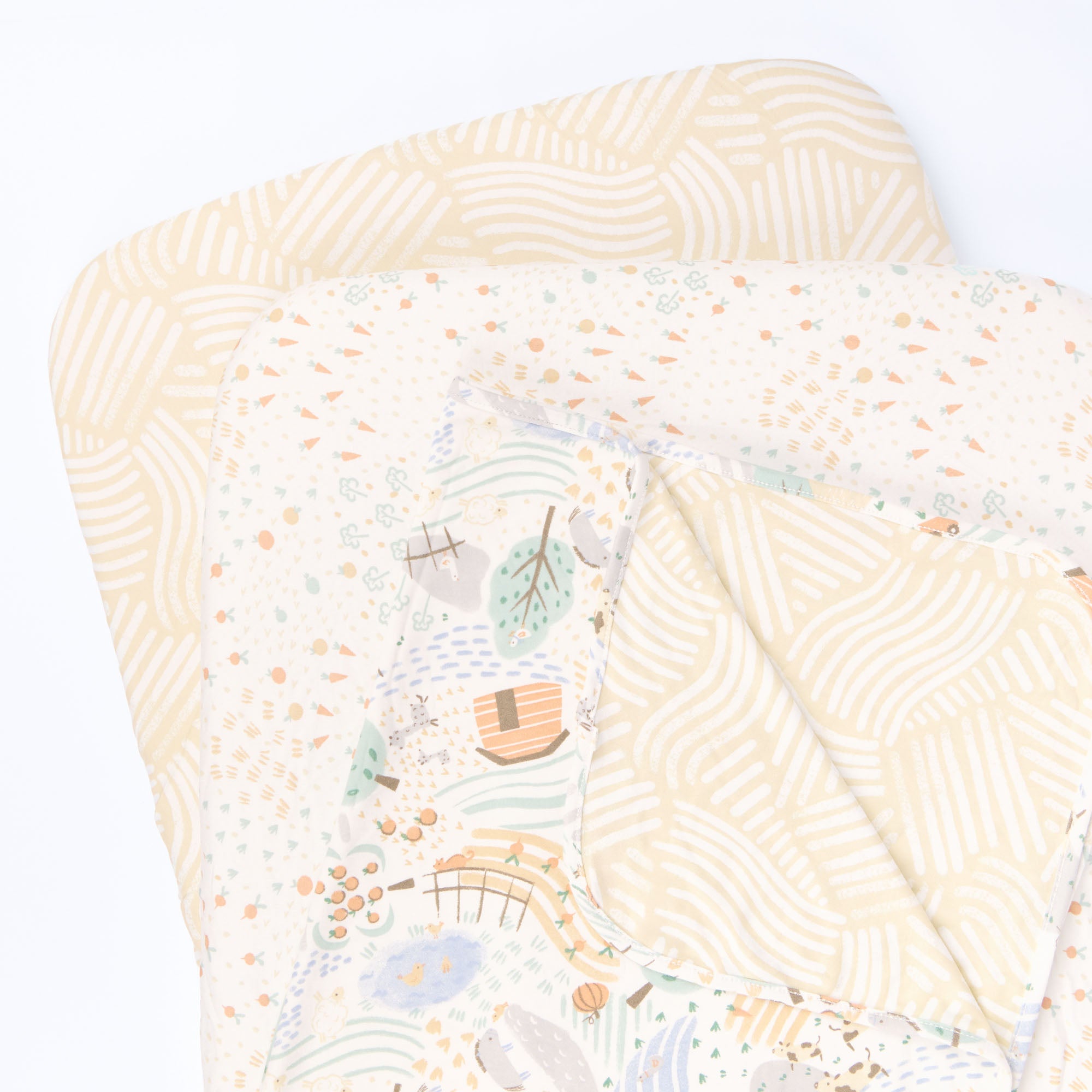 Cutout view of the Good Life bedside crib starter pack with two patterned fitted sheets and a reversible coverlet featuring playful farmyard motifs