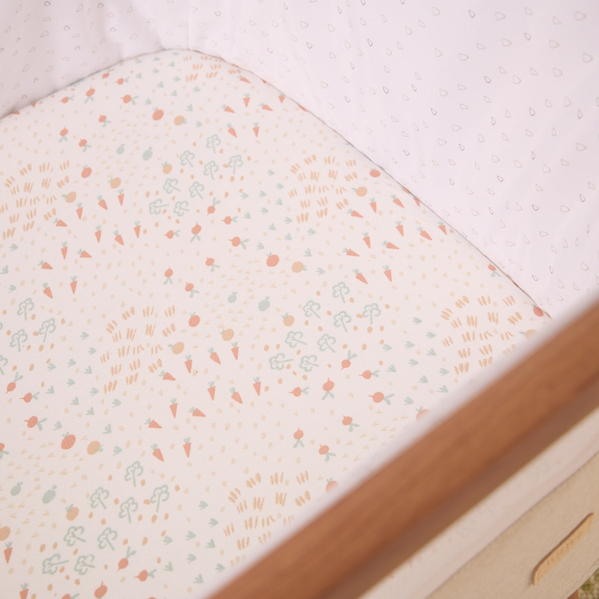 Close-up of the Good Life bedside crib fitted sheet in soft cream with playful vegetable and garden motifs 