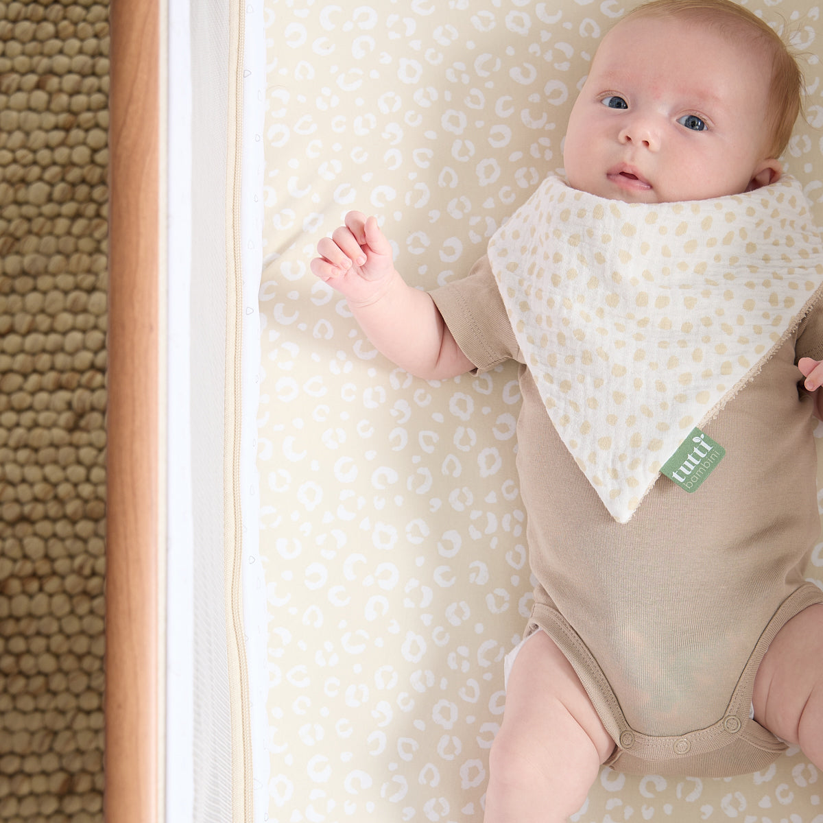 Baby lies peacefully on the Love Cats fitted sheet in warm beige tones, creating a calm and coordinated crib look