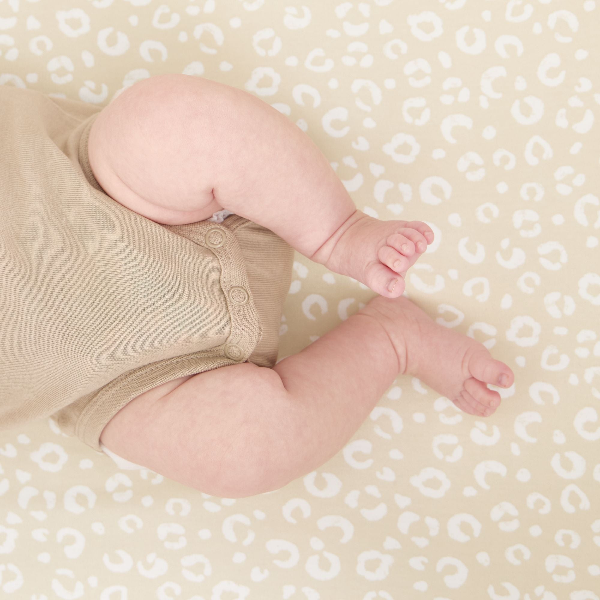 Baby legs in a beige outfit on the Love Cats crib fitted sheets