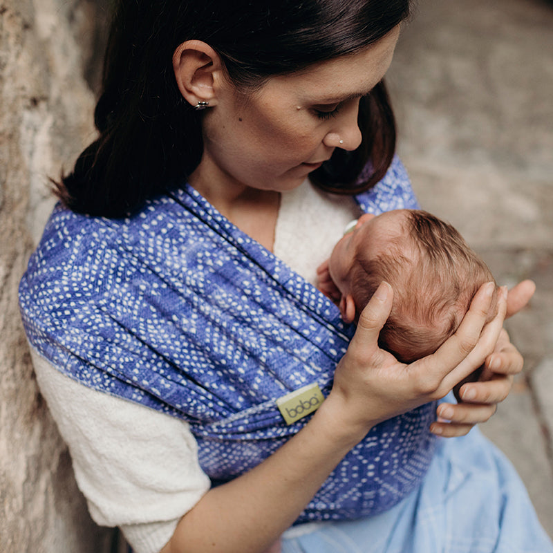 Woman holding a baby in a blue wrap against a natural background