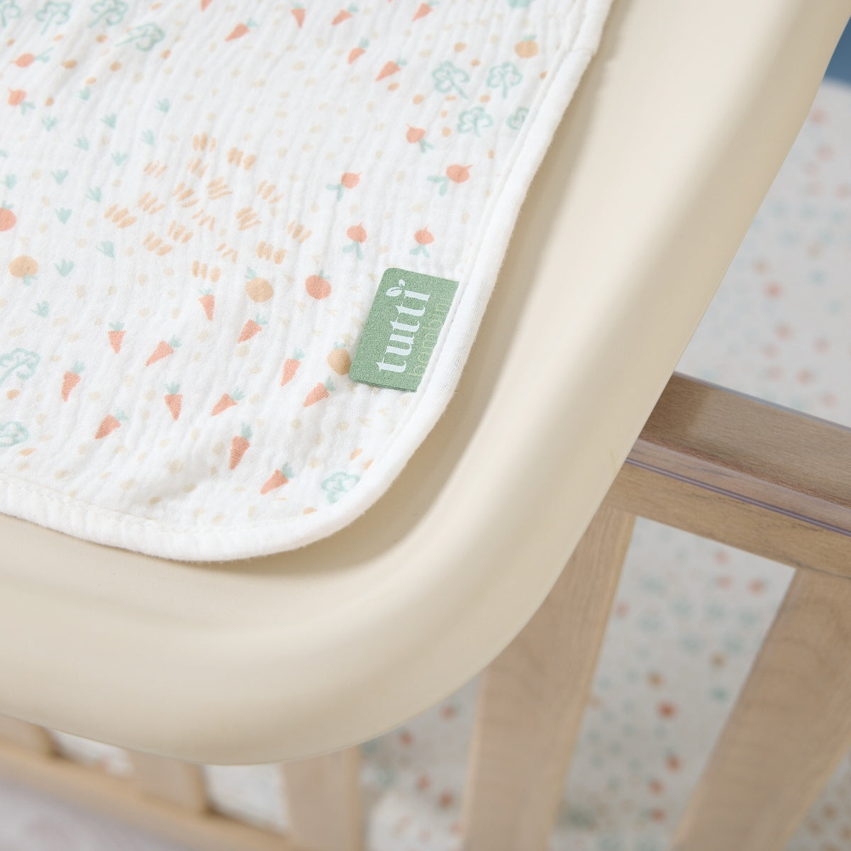 Close-up of muslin changing mat liner corner showing Tutti Bambini label and soft cream fabric with carrot and leaf print detail