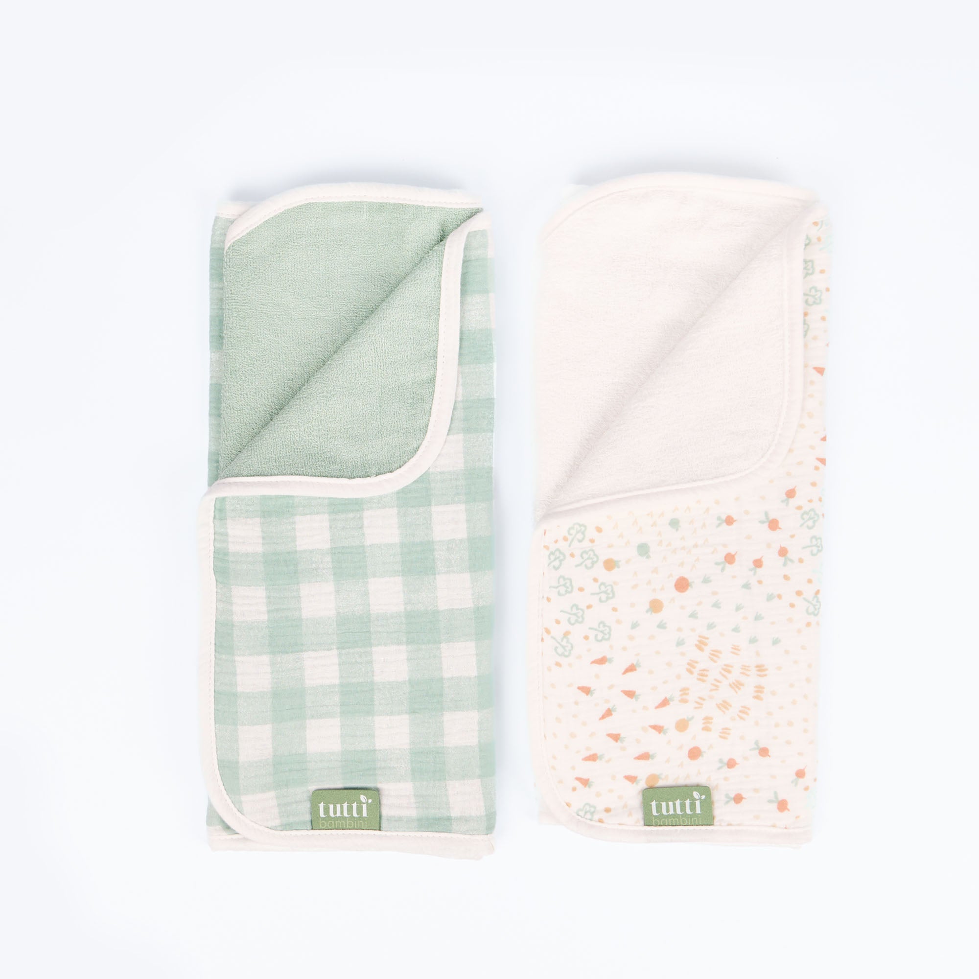 Cutout of two changing mat liners featuring reversible designs in green gingham and carrot print, made from soft, absorbent muslin