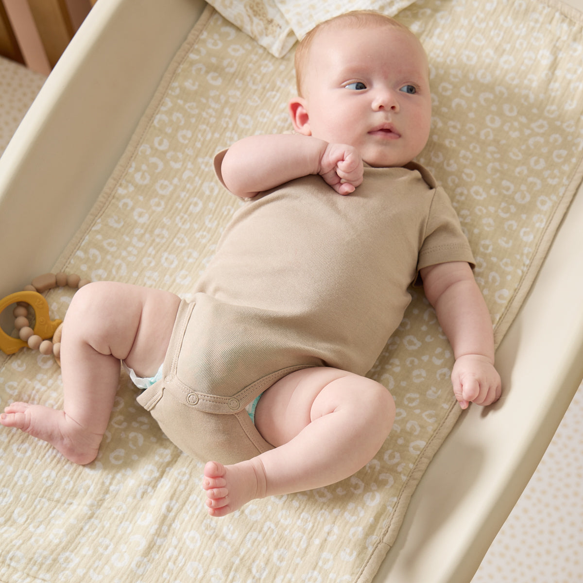 Baby lying comfortably on beige leopard print changing mat liner, highlighting the soft muslin fabric and calm, cosy nursery tones