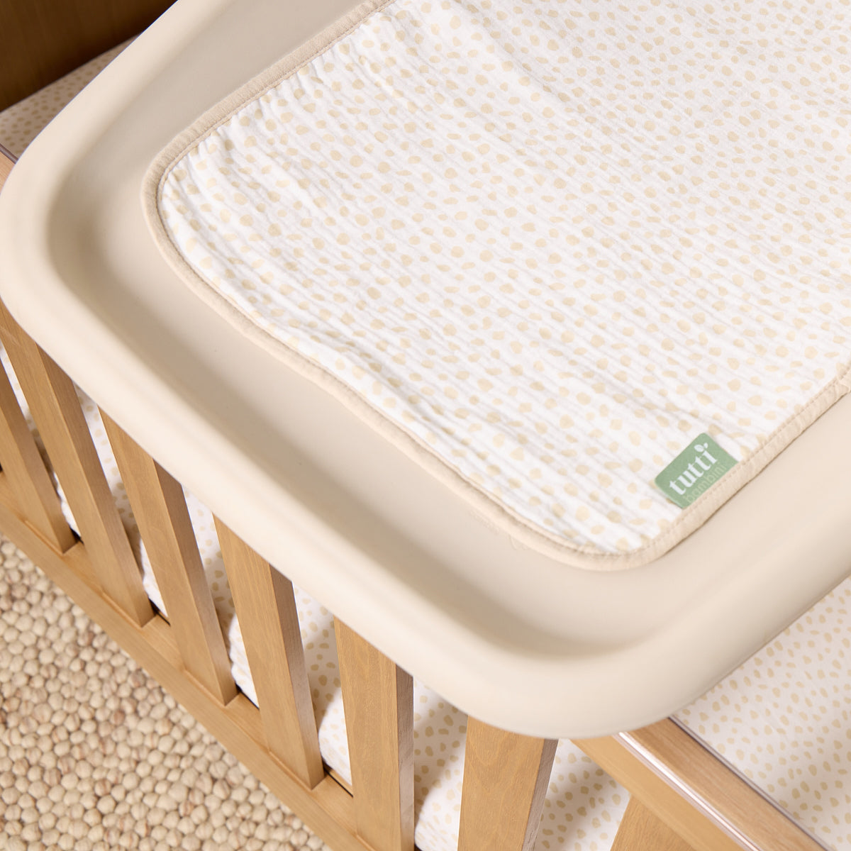 Soft muslin changing mat liner in cream and beige spot print styled on cot-top changer, blending seamlessly into a warm neutral nursery