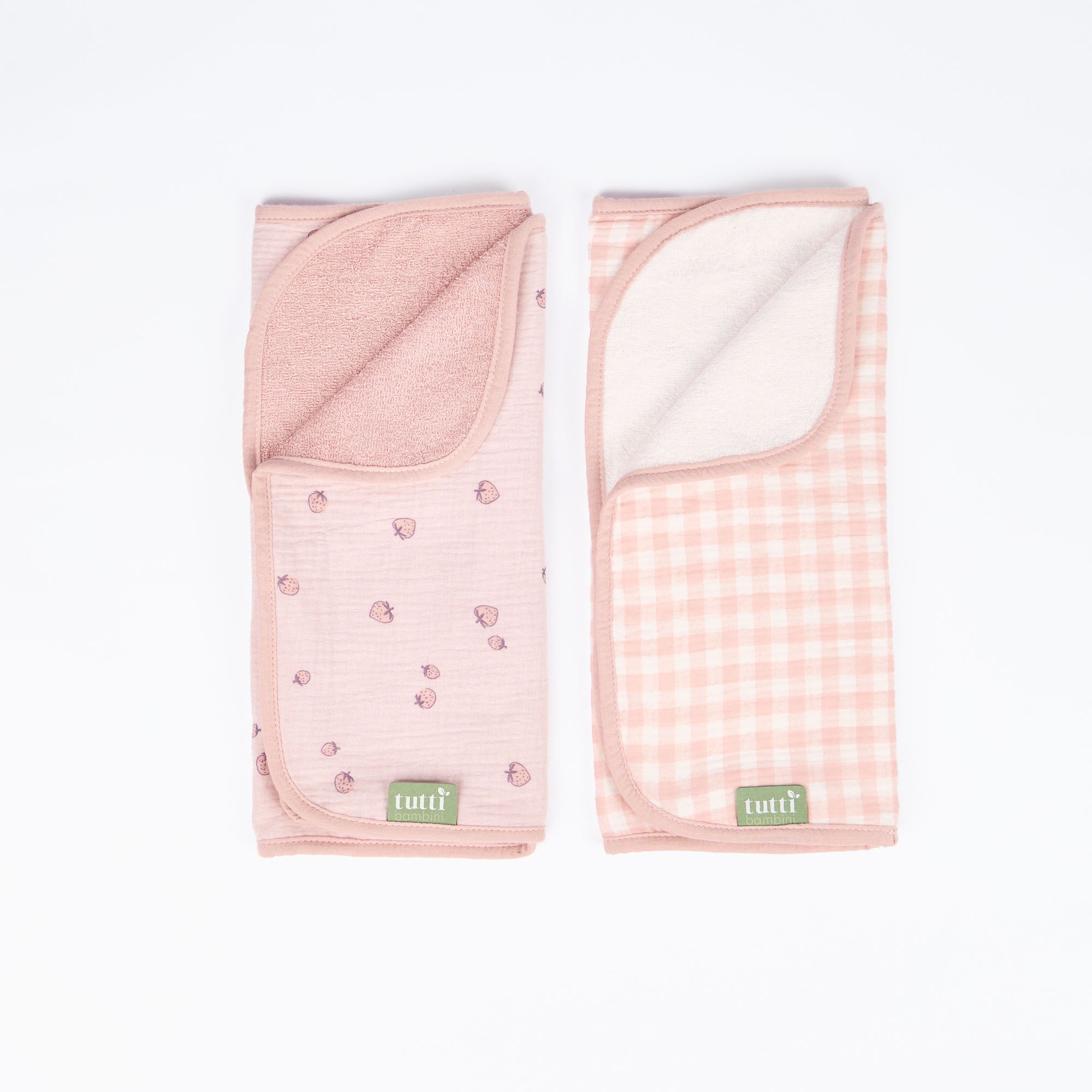 Cutout view of two pink changing mat liners featuring reversible strawberry and gingham designs made from soft, absorbent muslin fabric