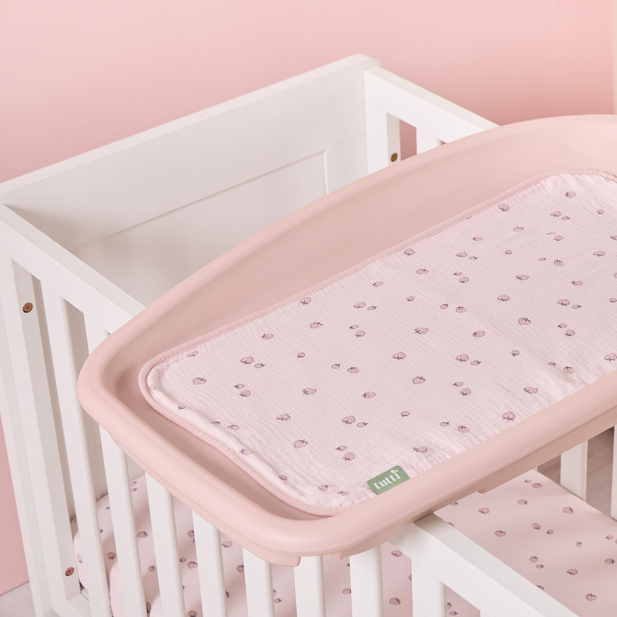Pink strawberry print changing mat liner styled on a cot-top changer against soft pink nursery tones