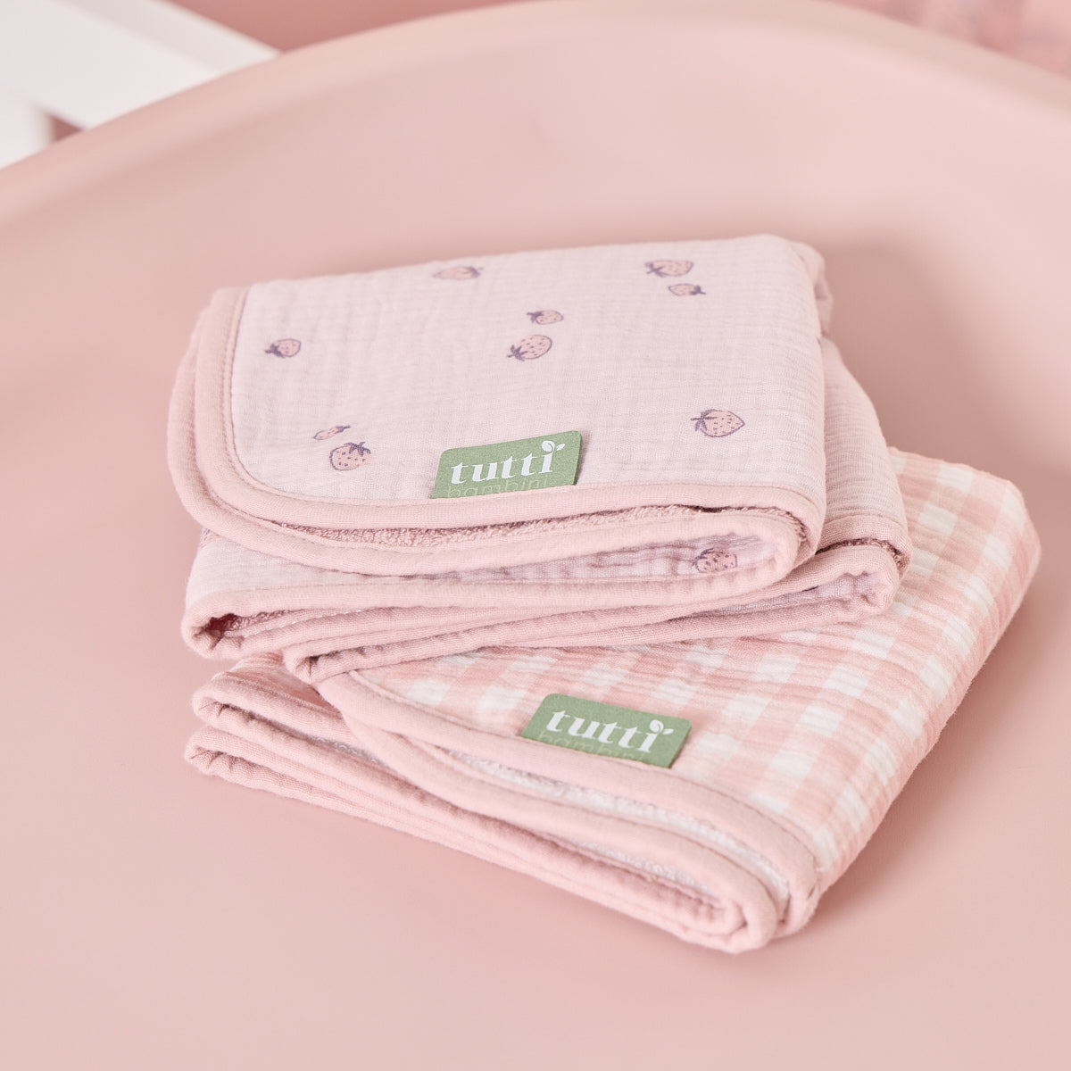 Folded pink changing mat liners in strawberry and gingham prints, crafted from soft muslin with absorbent towelling reverse