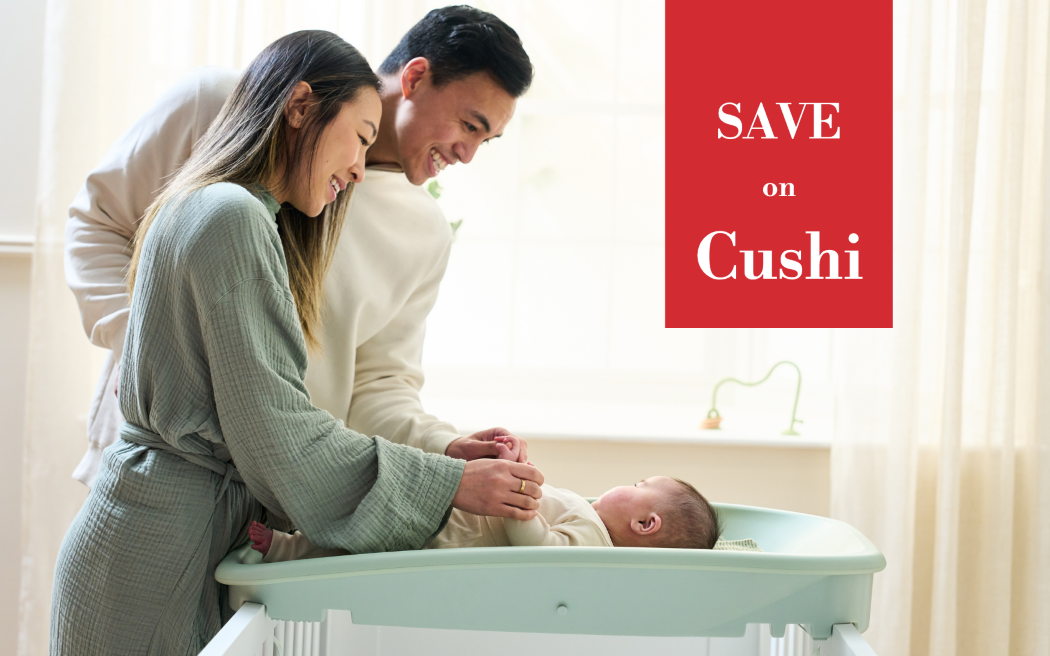 A family of three in a bright nursery setting, with a baby lying in a mint green Cushi changing mat while a man and woman lean over to look at the baby. A red promotional overlay on the right reads 'SAVE on Cushi'.