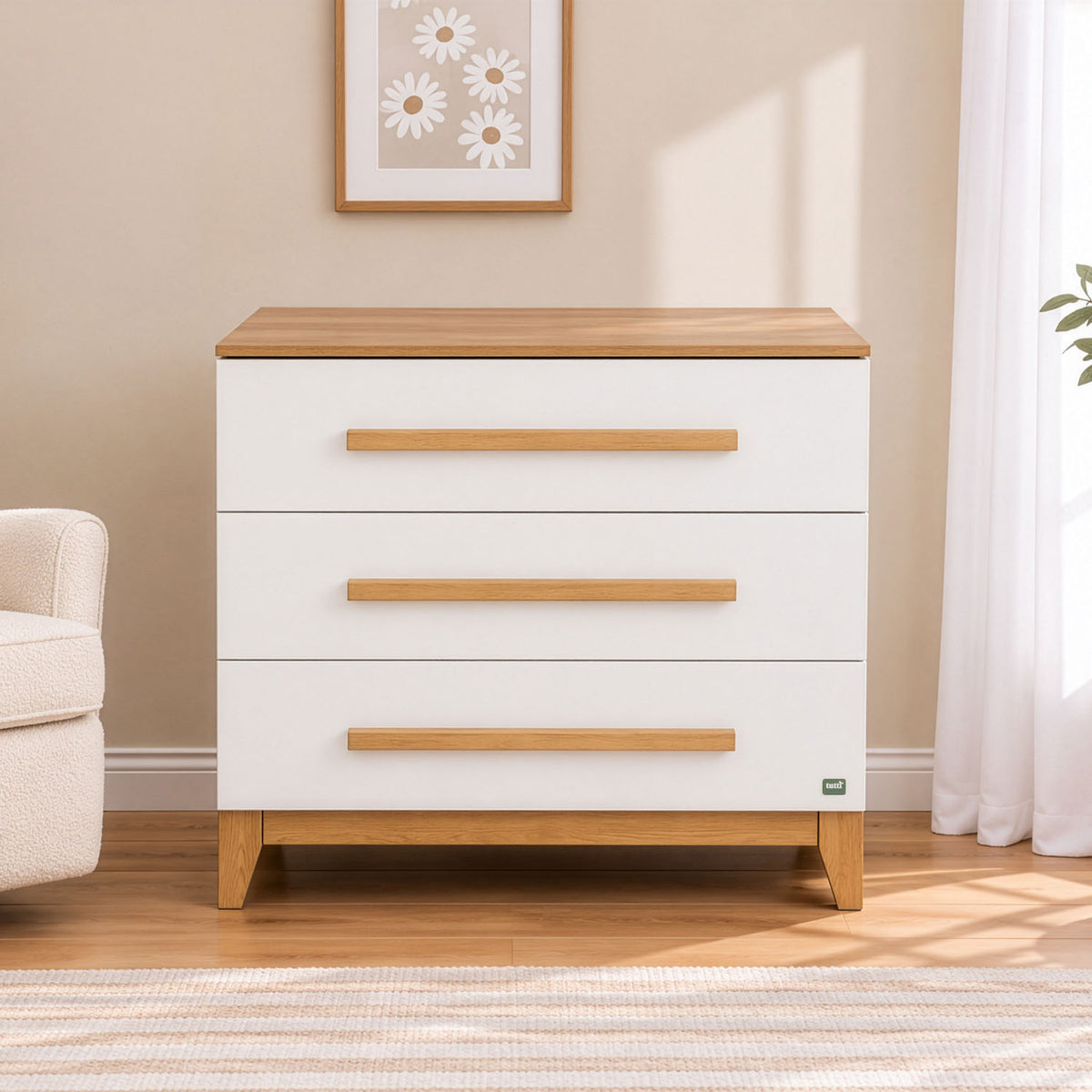A three-drawer chest of drawers with a golden oak wood top and matching wood drawer pulls, set against a beige wall with a window light casting soft shadows.