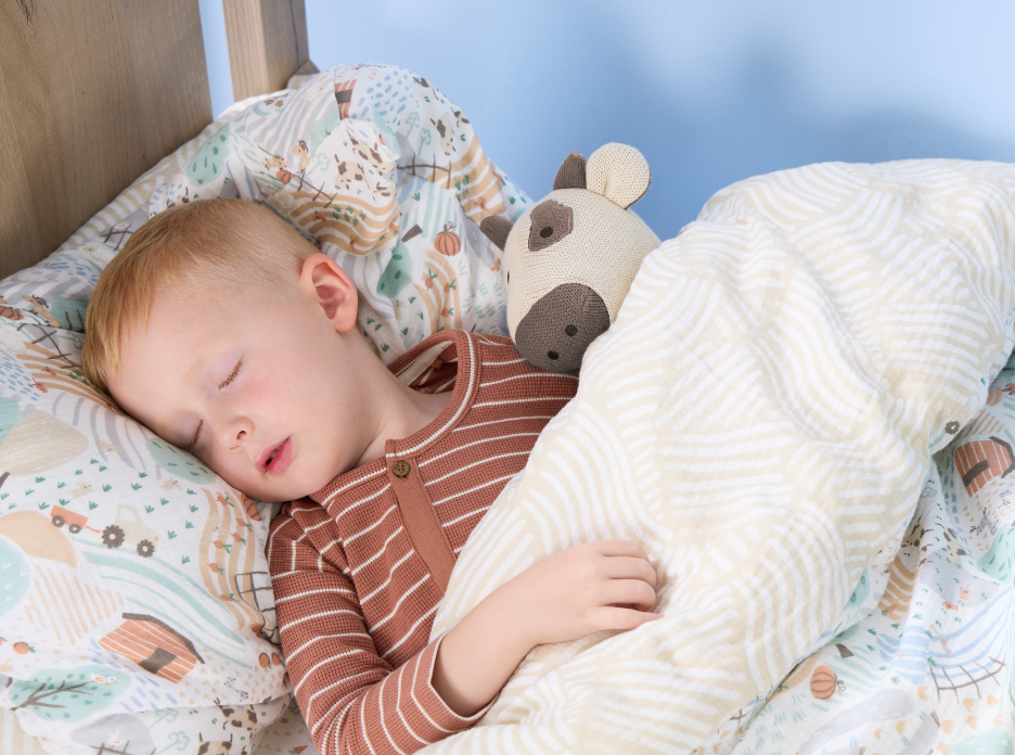 A child sleeping on a bed with Clemi Cow knitted toy