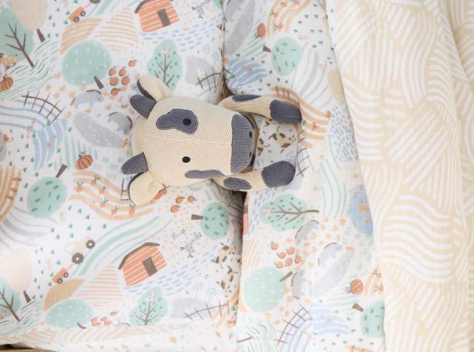 Clemi Cow cute knitted toy on a patterned blanket with a soft texture