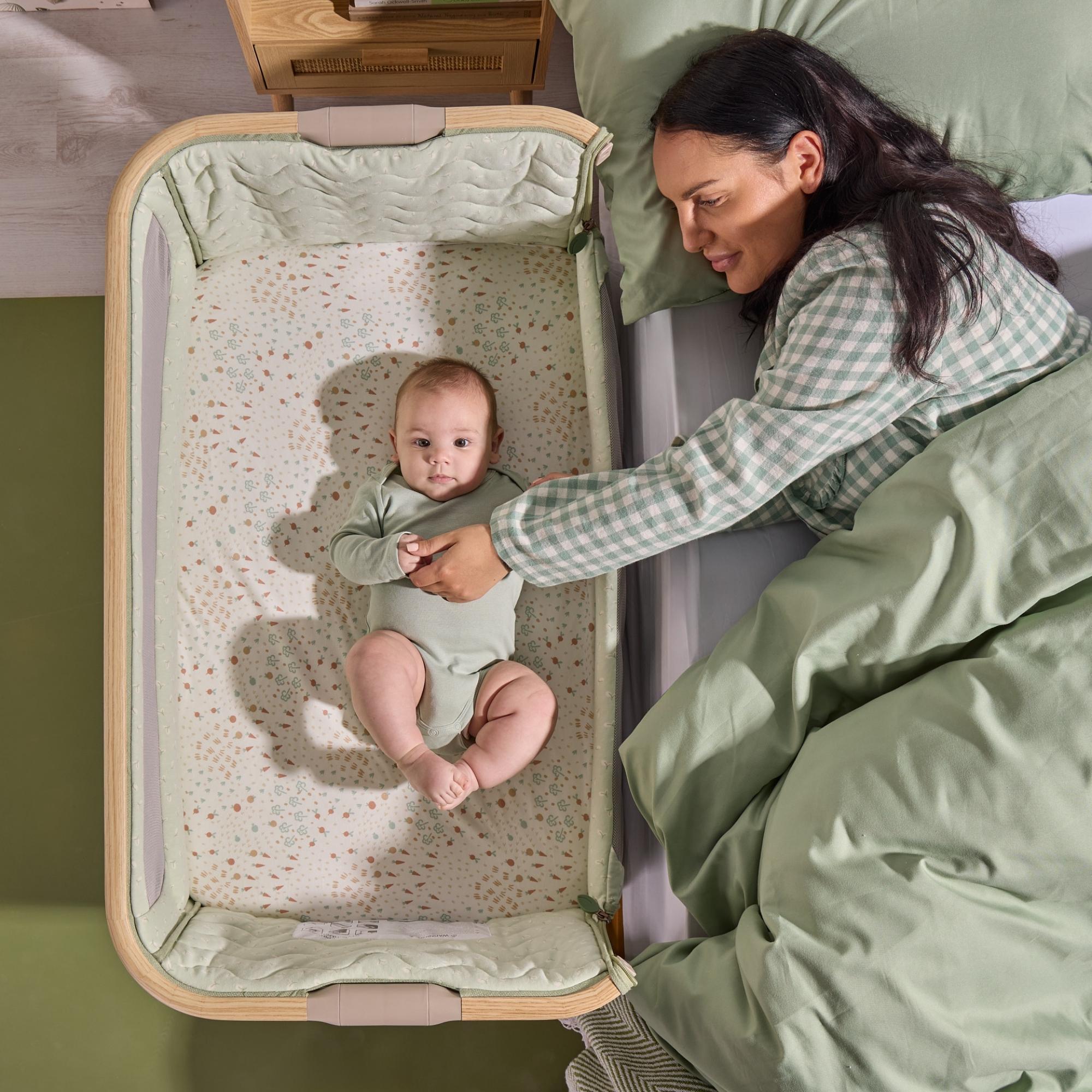 Overhead view of a baby resting in the CoZee Air 2 bedside crib in eucalyptus, positioned next to the bed for safe co-sleeping.