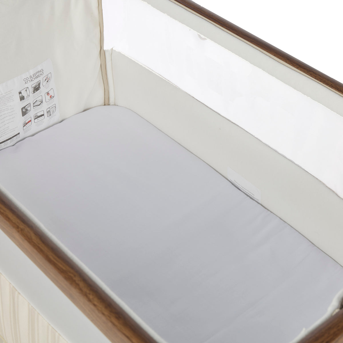 A white bedside crib fitted sheet covering a mattress inside a rich walnut and cashmere vintage stripe crib.